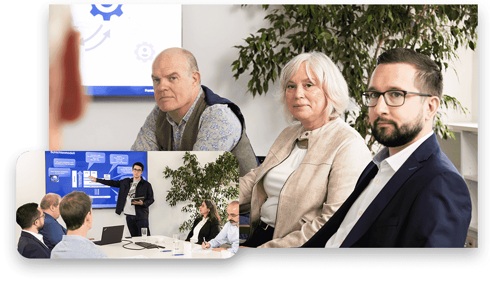 Personen rund um Konferenztisch und Präsentation am Bildschirm im Hintergrund